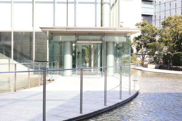アトリウムからの水盤に浮いたアプローチを越えてエントランスへ誘います。		