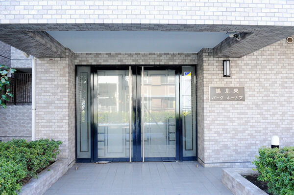 【鶴見東パーク・ホームズ】両側の植栽とガラスの扉が透明感ある明るい雰囲気を醸し出すエントランス。